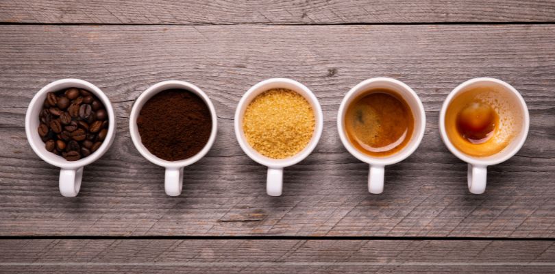 Five mugs filled with coffee beans, sugar, and coffee.