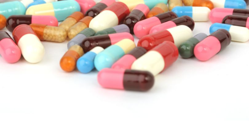 A variety of different pills, all different colors, on a white background.